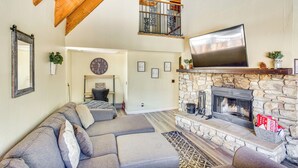 A living room with a stone fireplace, a large flat-screen TV, and a cozy seating area. - 7 Mi to Big Bear Lake: A-frame Home w/ Deck! (Sugarloaf)