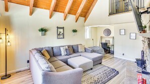 A spacious living room with a large sectional sofa, wooden beams on the ceiling, a staircase to an upper level, and a fireplace. - 7 Mi to Big Bear Lake: A-frame Home w/ Deck! (Sugarloaf)