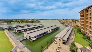 A marina with docked boats, a building with multiple balconies, and a grassy area with outdoor seating. - Lake LBJ Condo w/ Private Balcony, Lake Views (Horseshoe Bay)