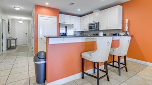 A modern kitchen with white cabinets, a stainless steel refrigerator, a microwave, and two bar stools. - Lake LBJ Condo w/ Private Balcony, Lake Views (Horseshoe Bay)