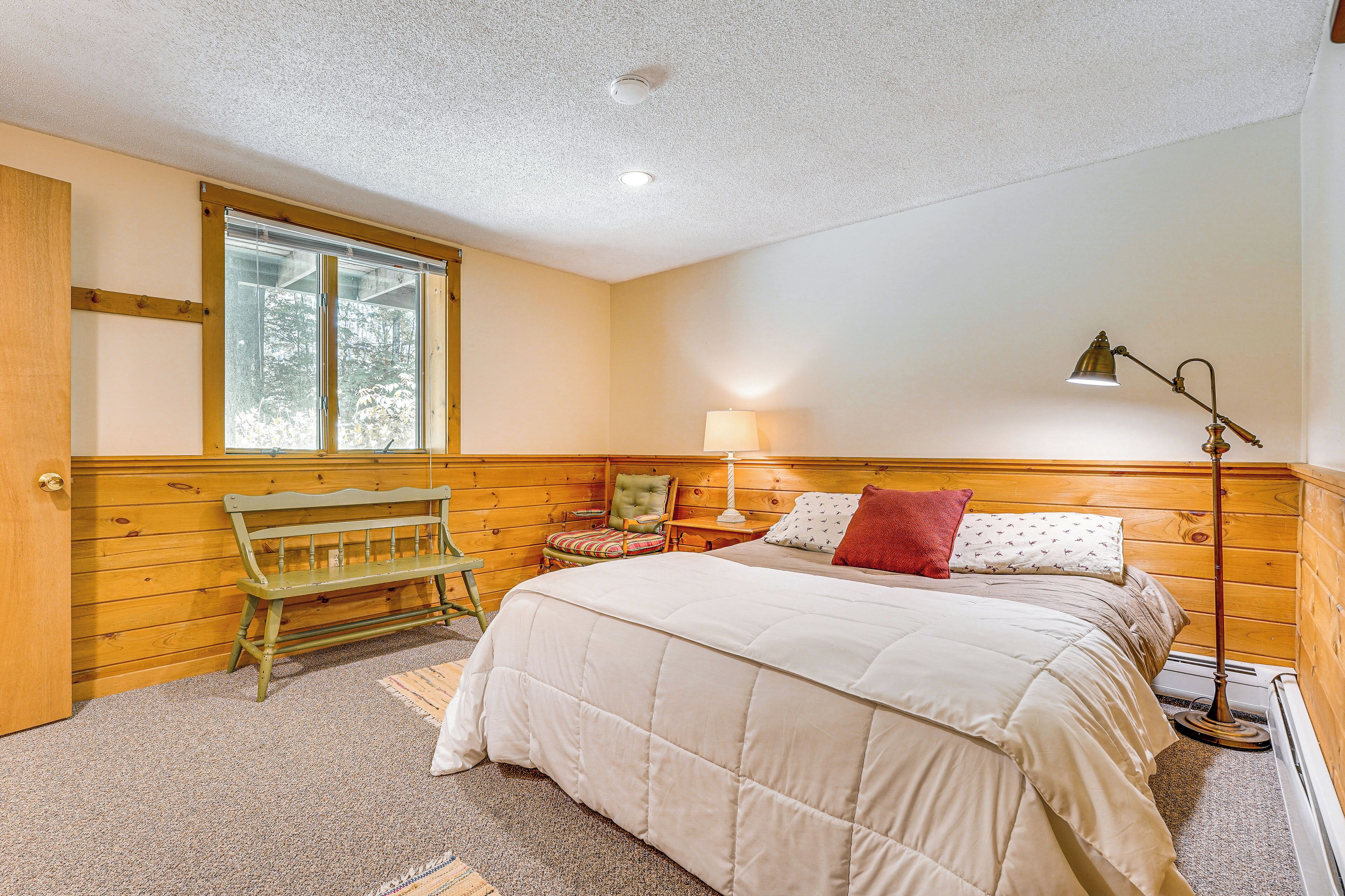 A bedroom with a bed, a bench, a chair, a lamp, and a window.