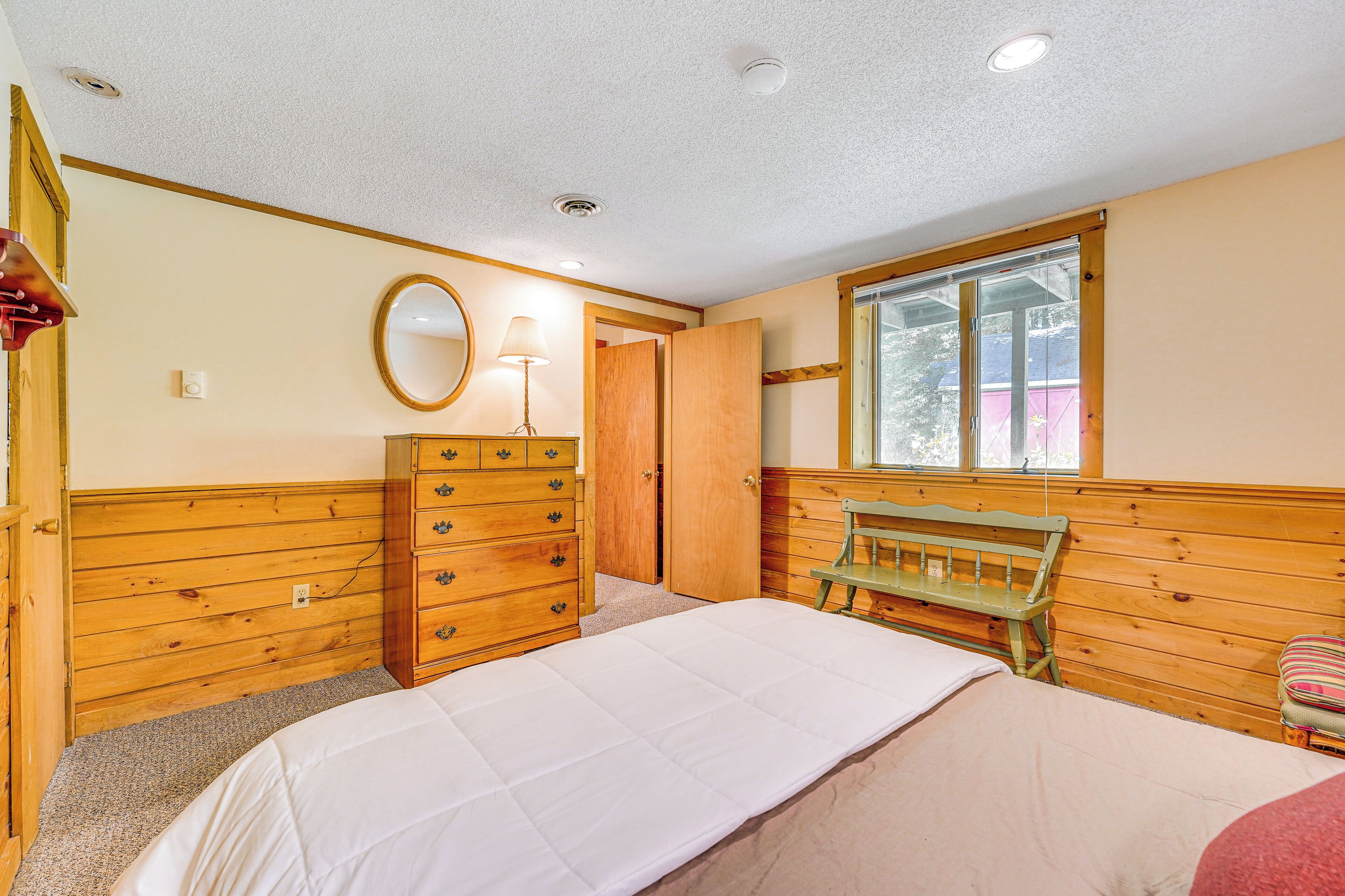 A bedroom with a bed, wooden dresser, and a window with a view.