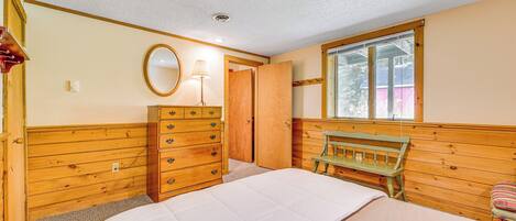 A bedroom with a bed, wooden dresser, and a window with a view.