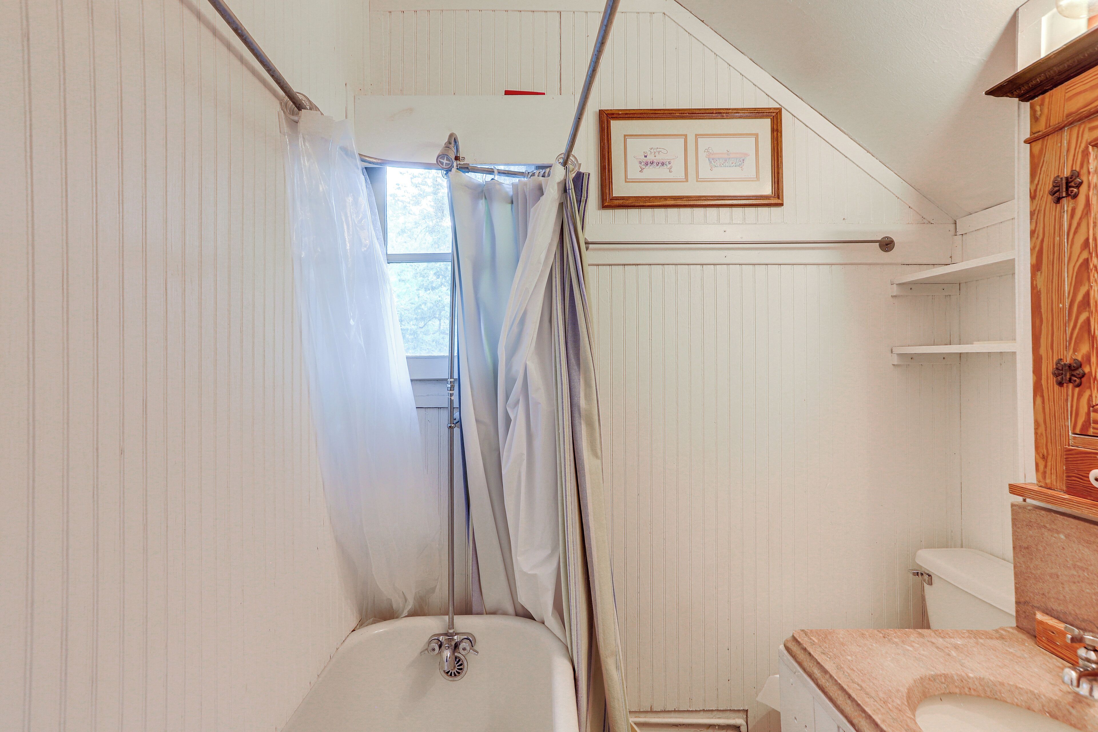 A bathroom with a bathtub, a window with curtains, and wooden shelves.