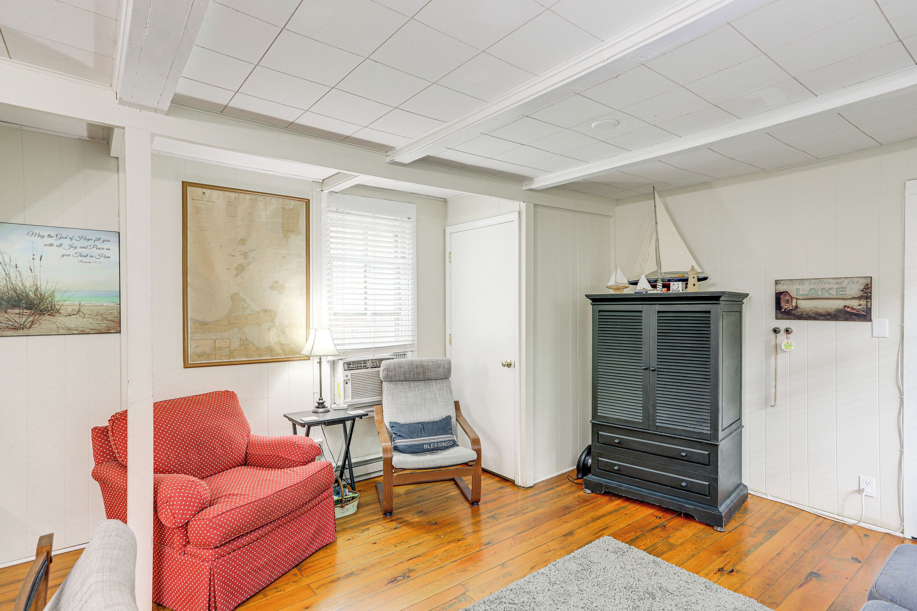 Une pièce avec un plancher en bois, un canapé rouge à pois, un fauteuil gris, une commode et un tableau accroché au mur.