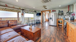 A spacious living room with a leather sofa, wooden coffee table, and a kitchen area with a refrigerator, oven, and various kitchen items. - Waterfront Perry Home: Rooftop Deck, Pets Welcome! (Perry)