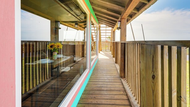 A wooden deck with glass railings, a table with a vase of sunflowers, and a view of the sky. - Waterfront Perry Home: Rooftop Deck, Pets Welcome! (Perry)