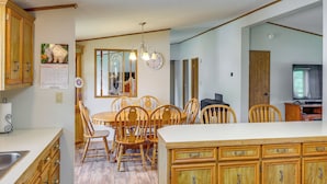 A kitchen with wooden cabinets, a dining table with chairs, a chandelier, and a clock on the wall. - Kadoka Home ~ 22 Mi to Badlands National Park! (Kadoka)
