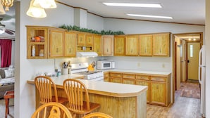 A kitchen with wooden cabinets, a central island with chairs, a stove, and a microwave. - Kadoka Home ~ 22 Mi to Badlands National Park! (Kadoka)