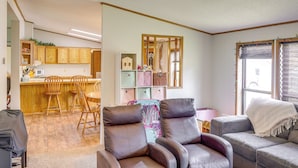 A living room with a grey sofa, a brown leather chair, and a dining area with wooden chairs and a kitchen in the background. - Kadoka Home ~ 22 Mi to Badlands National Park! (Kadoka)