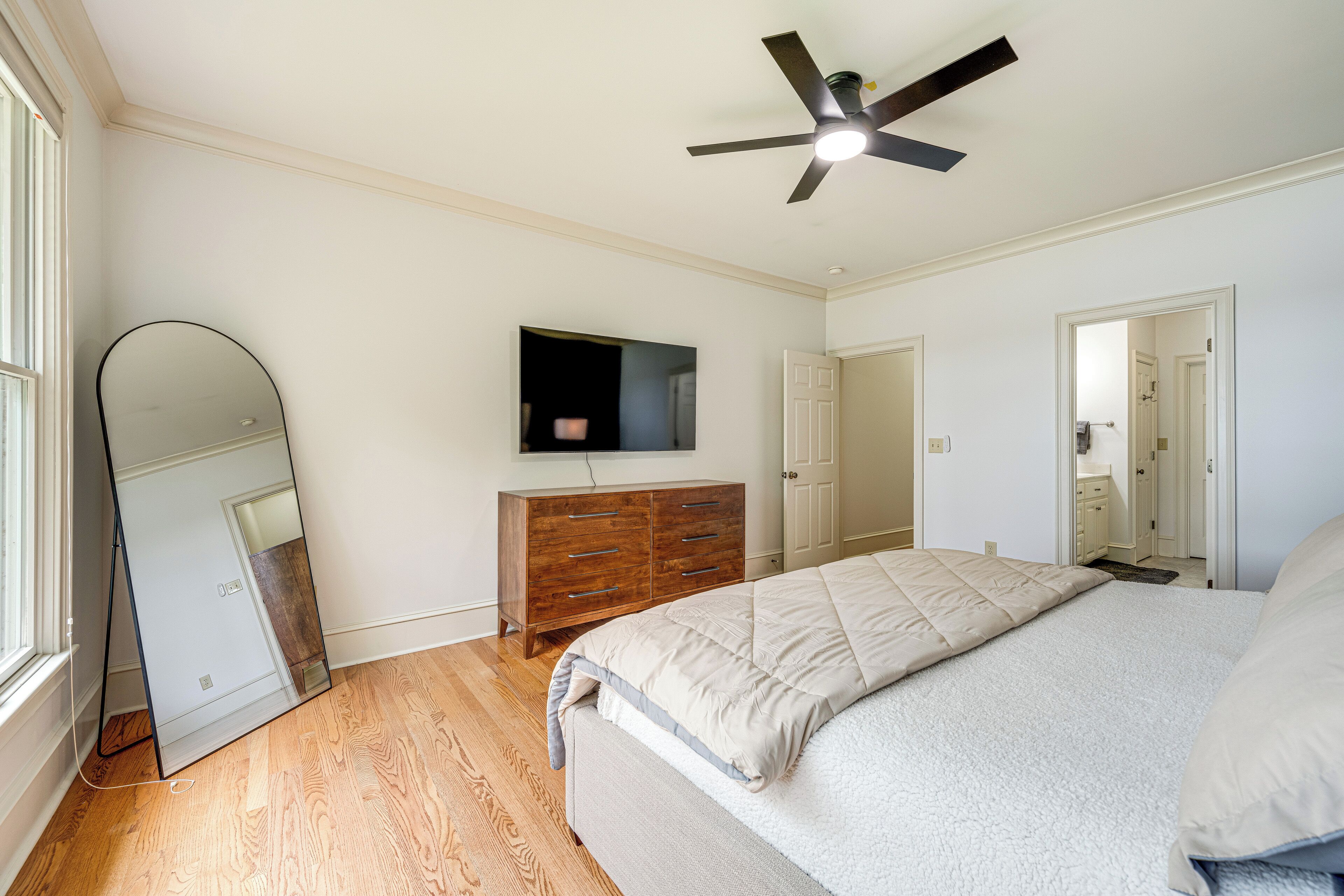 A bedroom with a bed, a wooden dresser, a TV, and a ceiling fan.