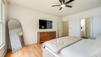 A bedroom with a bed, a wooden dresser, a TV, and a ceiling fan.