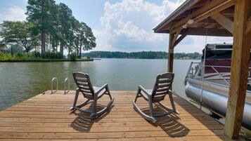 A wooden deck with rocking chairs and a covered area overlooking a lake.