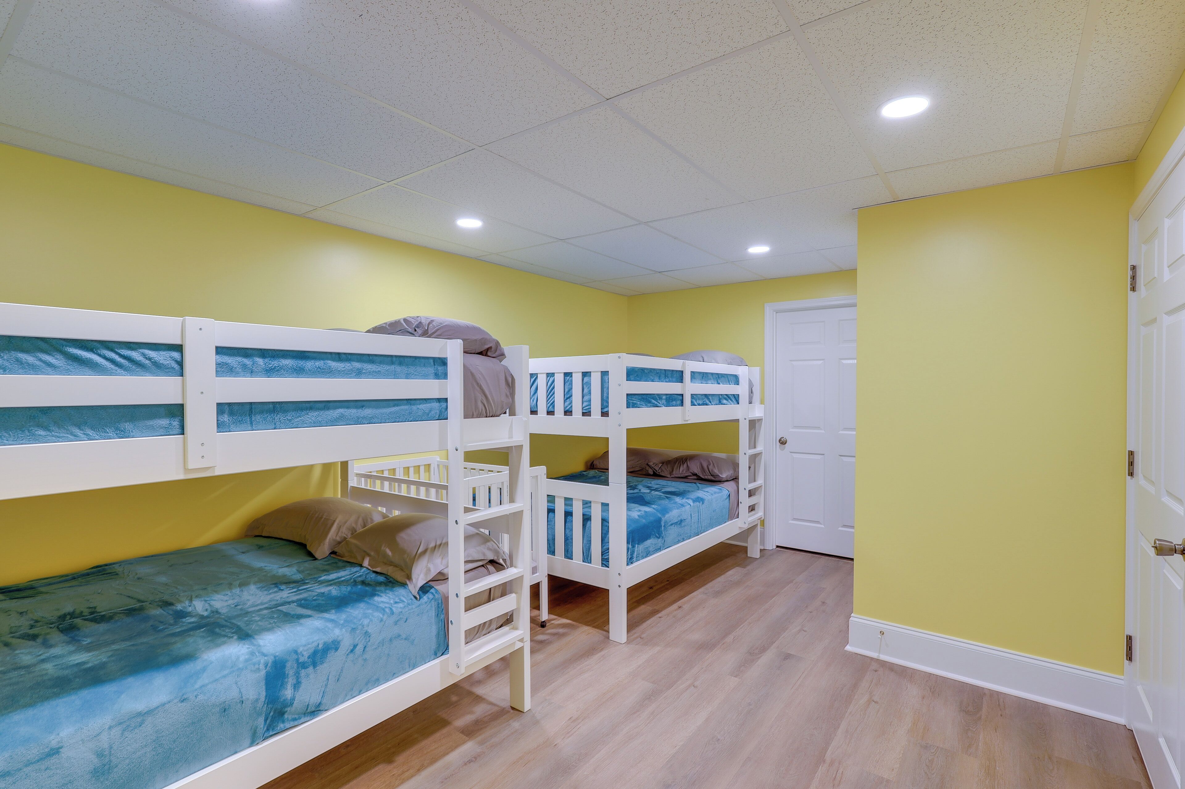 A room with three bunk beds, yellow walls, and a wooden floor.