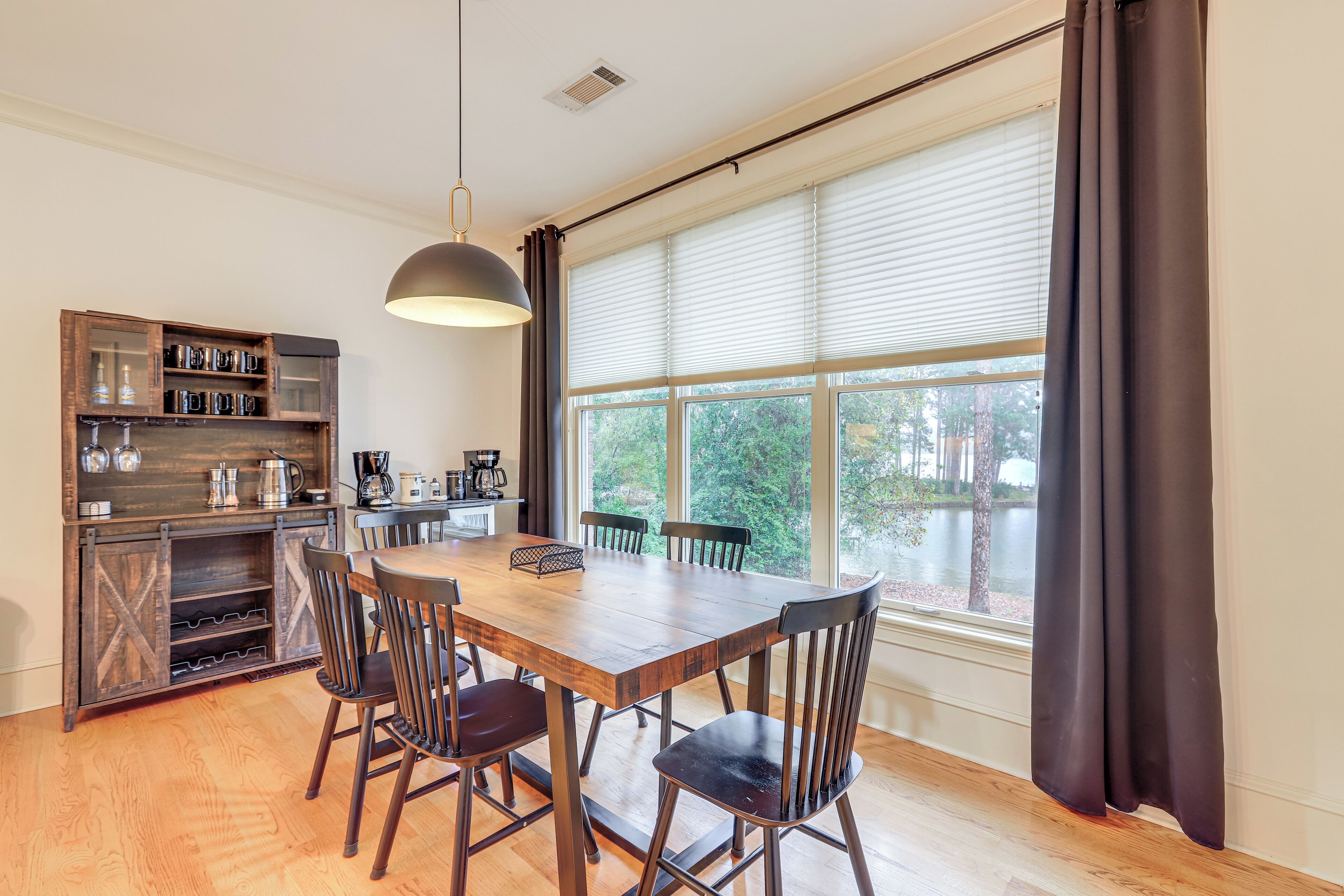 A dining area with a wooden table and chairs, a built-in wine rack, and a view of a lake through large windows.