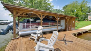 A wooden dock with a covered seating area, a boat, and a small building.