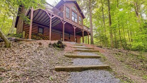 A wooden cabin with a porch, surrounded by a forest.