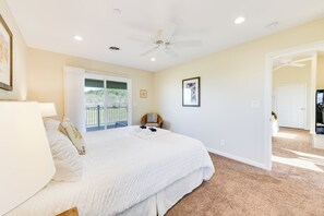 A bedroom with a large bed, a ceiling fan, a door leading to a balcony, and a framed picture on the wall.
