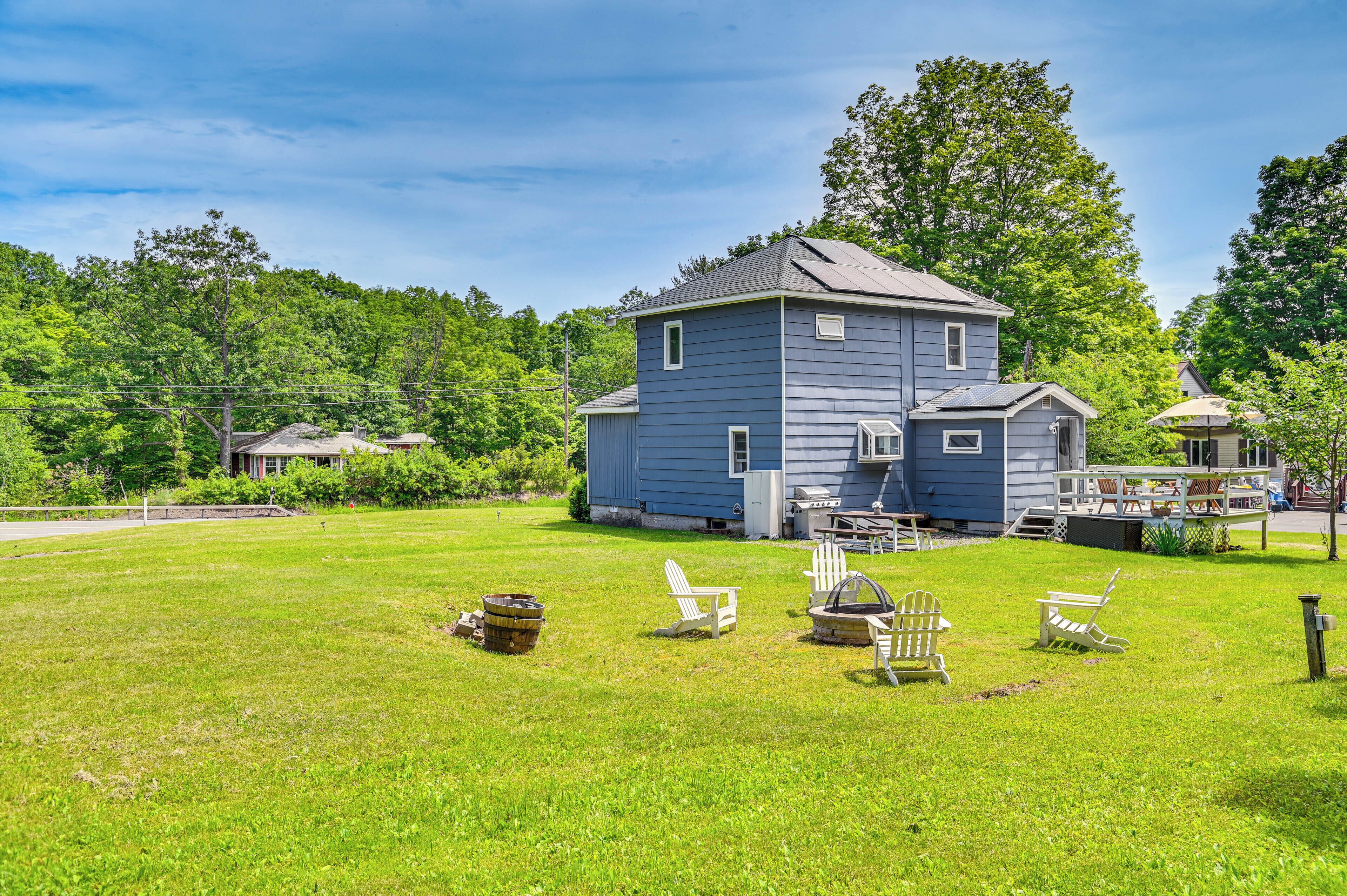 A large blue house with a deck, surrounded by a grassy yard and trees.