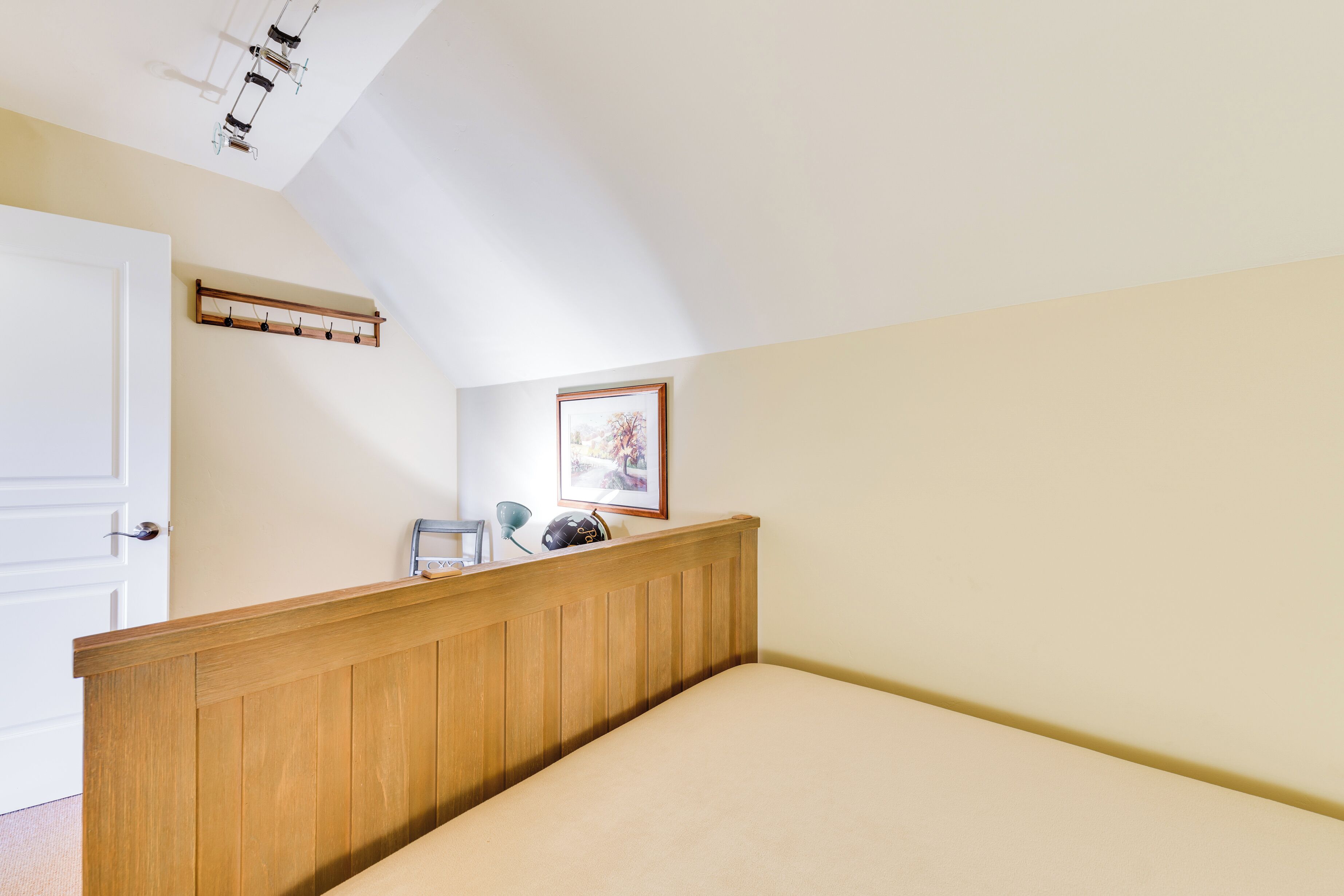 A bedroom with a sloped ceiling, a wooden headboard, a bed, a coat rack, a framed picture, and a door.