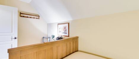 A bedroom with a sloped ceiling, a wooden headboard, a bed, a coat rack, a framed picture, and a door.