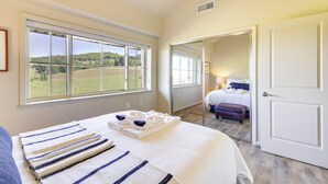 Habitación de hotel con una cama grande, vistas al campo, baño con espejo y una puerta que da a otra habitación.