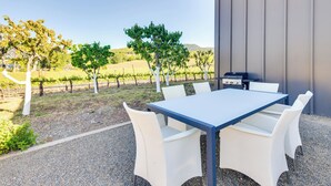 Un patio al aire libre con mesa y sillas, una parrilla y vistas a un viñedo.