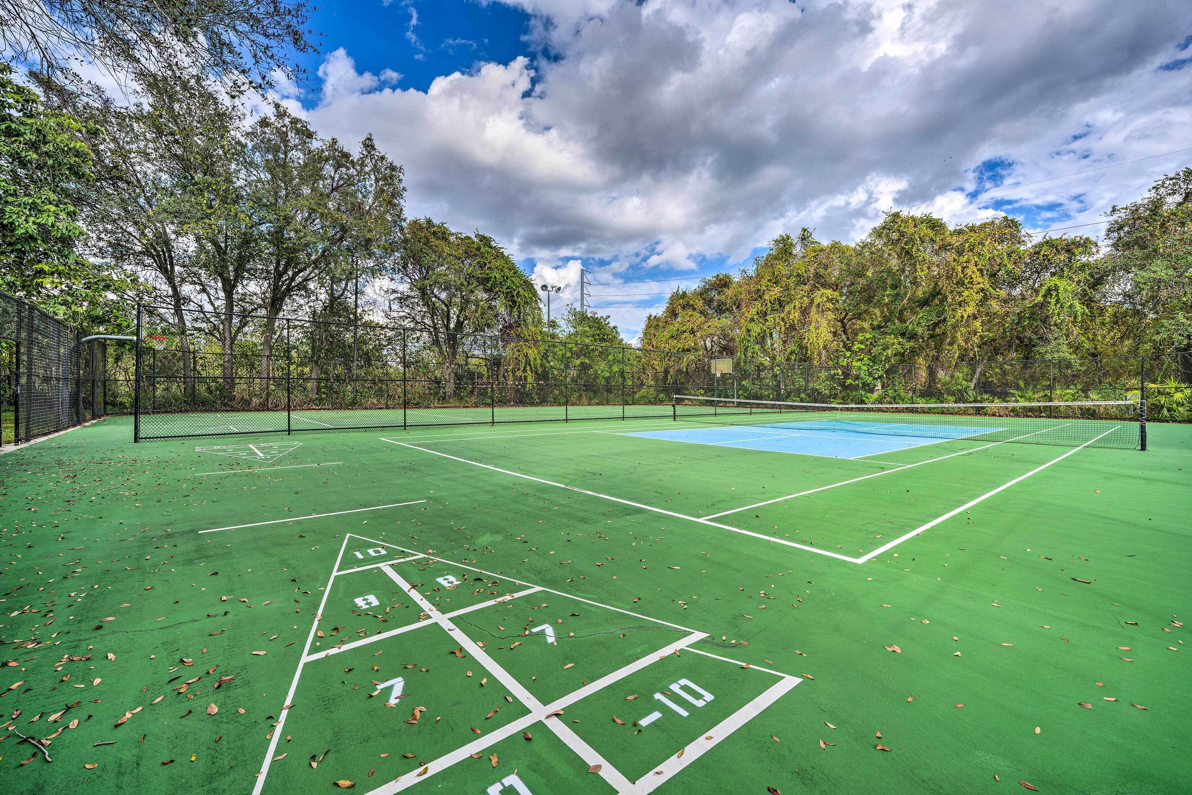 A green outdoor court with a shuffleboard area, surrounded by trees and a clear sky.