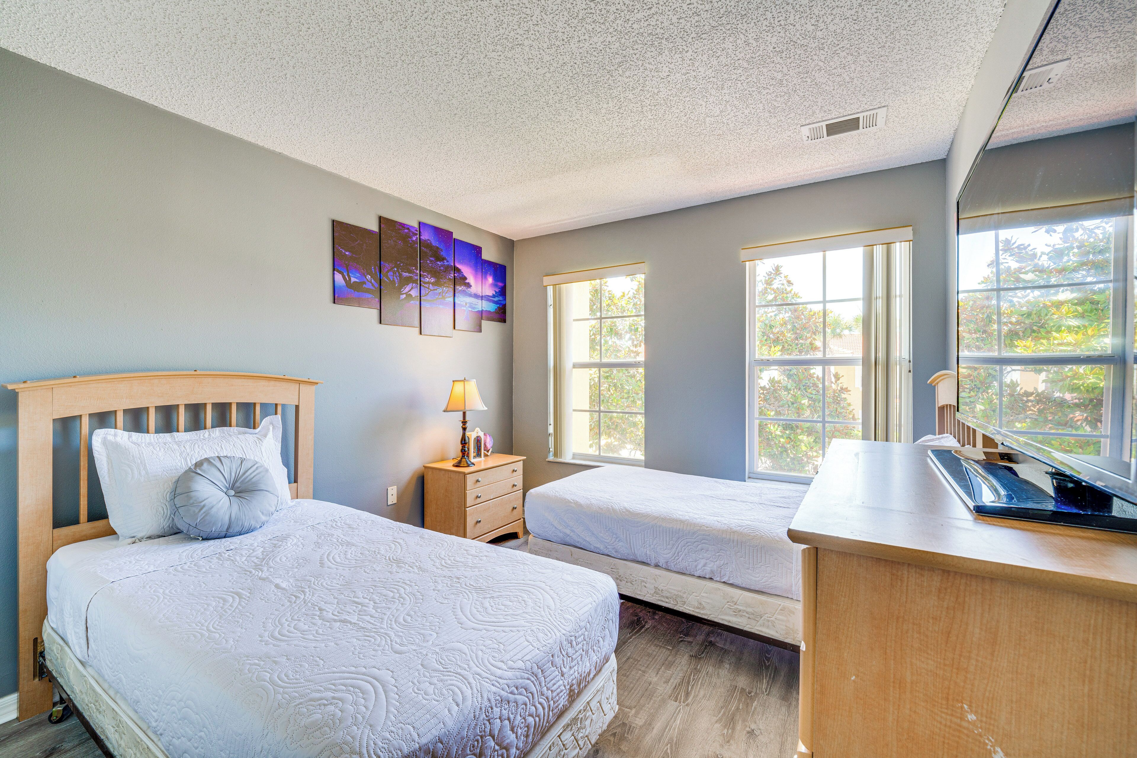 A bedroom with two beds, a nightstand, a desk, and a window with a view of trees.