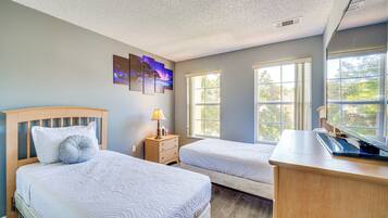 A bedroom with two beds, a nightstand, a desk, and a window with a view of trees.