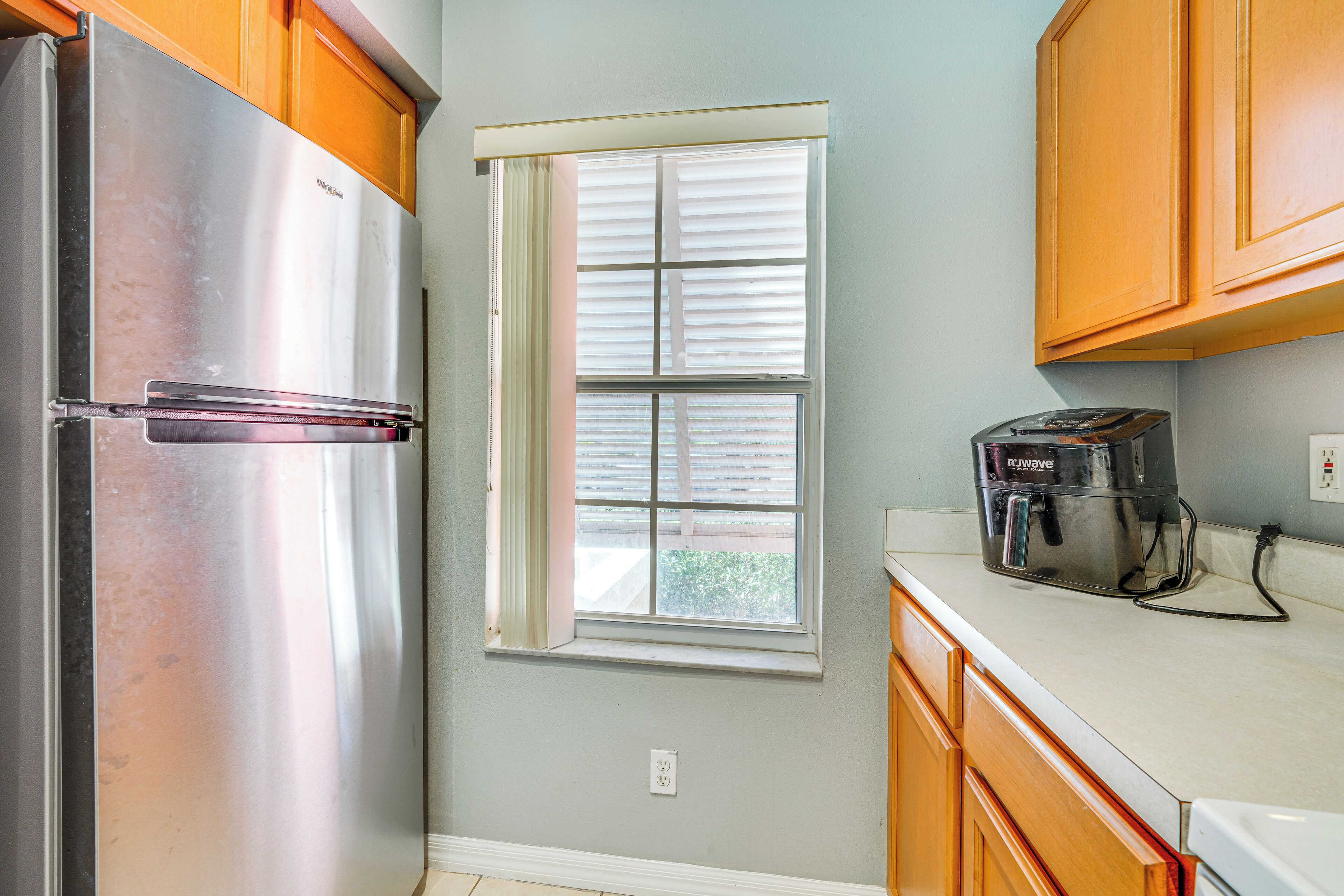 A kitchen with a stainless steel refrigerator, a window with blinds, wooden cabinets, and a coffee maker on the counter.