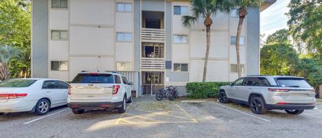 A parking lot with three vehicles, a building with a central entrance, and a palm tree.
