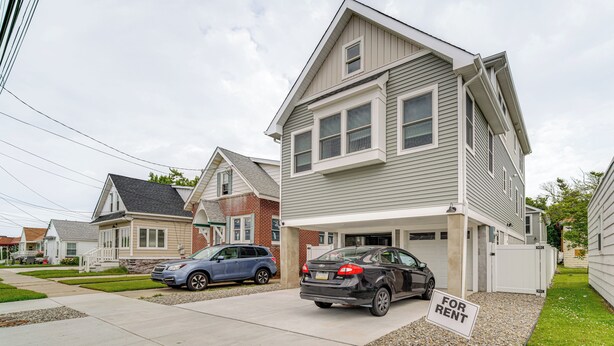A two-story house with a garage, a 'For Rent' sign, and two cars parked in the driveway.
