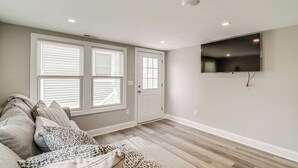 A living room with a sofa, a flat-screen TV mounted on the wall, and a door with a window.