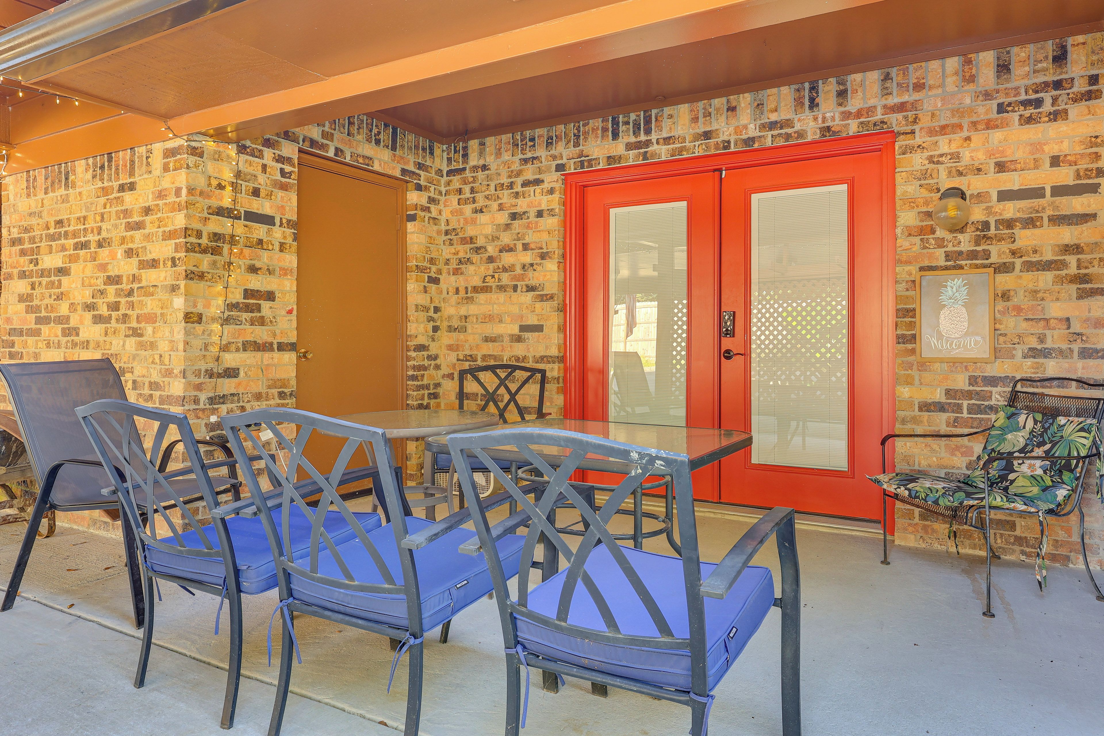 An outdoor patio with a brick wall, a red door, and blue chairs.