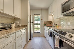 Een moderne keuken met witte kasten, een ingebouwde oven, een magnetron en een groot raam voor natuurlijk licht.