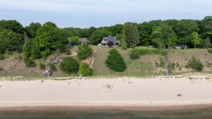 Een strand met een houten looppad dat naar een huis leidt, met een grote boom ervoor.