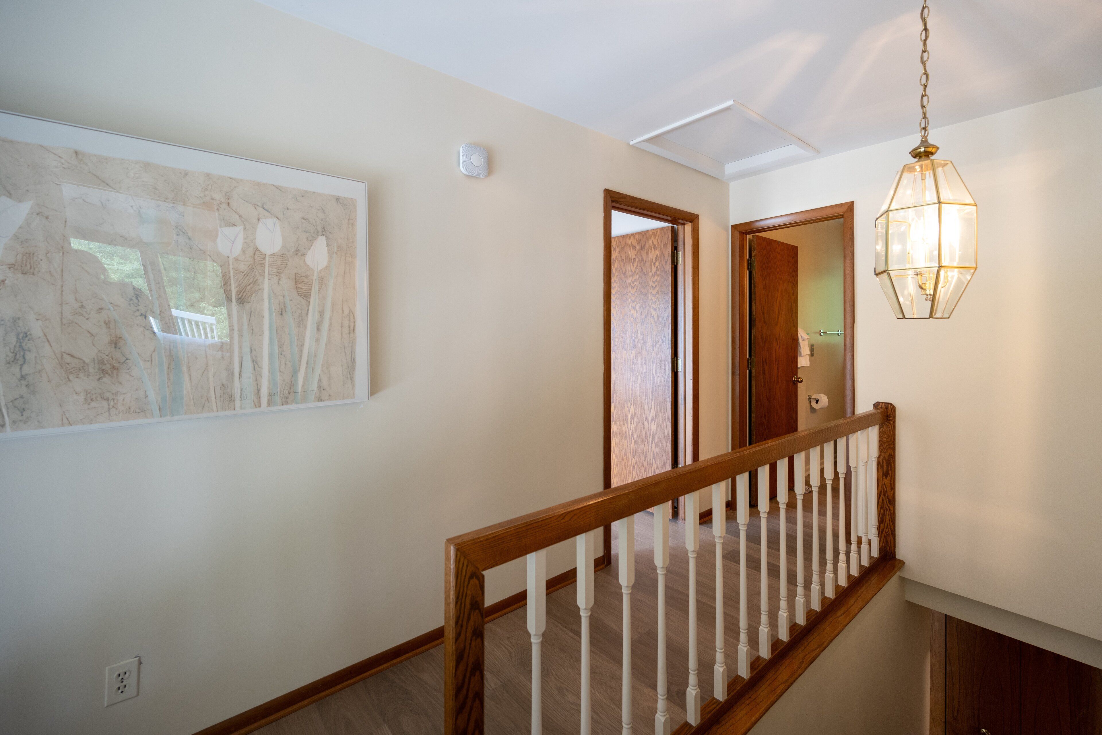 A hallway with a wooden staircase, a hanging light fixture, and a framed artwork on the wall.