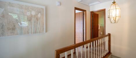 A hallway with a wooden staircase, a hanging light fixture, and a framed artwork on the wall.
