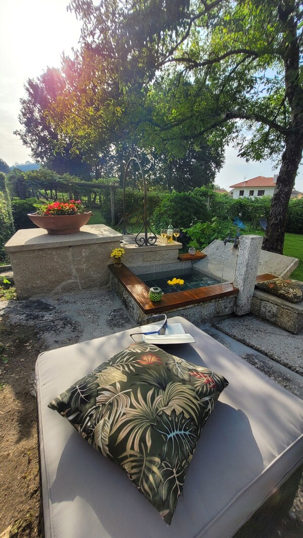 Un espace extérieur aménagé avec un banc rembourré, une petite table ornée d’un vase de fleurs et une arche décorative en métal.