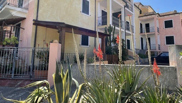 A multi-story residential building with balconies, a covered entrance, and a garden with plants and flowers. - Affittimoderni Valledoria - Sa Turritta (Valledoria)