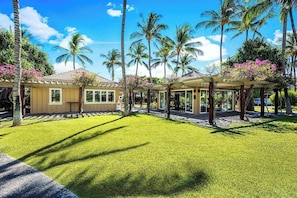 Un resort con una zona exterior cubierta, palmeras y un césped bien cuidado.