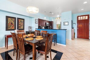 Un comedor con mesa y sillas de madera, una cocina con armarios oscuros y una pared azul de acento.