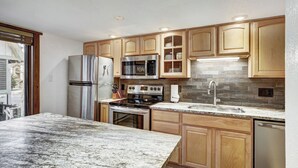 A modern kitchen with wooden cabinets, stainless steel appliances, and a granite countertop. - Stylish and convenient to town and the slopes! Lances West 11 (Breckenridge)