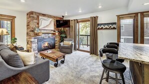 A cozy living area with a stone fireplace, a comfortable sofa, a coffee table, and a bar with stools. - Stylish and convenient to town and the slopes! Lances West 11 (Breckenridge)
