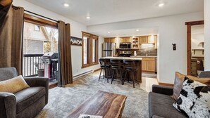 A modern living room with a fireplace, a dining area with bar stools, and a kitchen with wooden cabinets and stainless steel appliances. - Stylish and convenient to town and the slopes! Lances West 11 (Breckenridge)