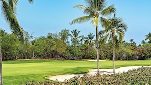 Ein Golfplatz mit einem gepflegten Grün, Sandbunkern und Palmen.