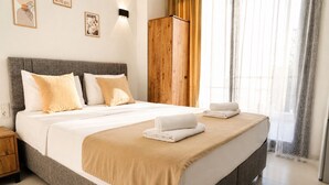 A neatly made bed with a grey headboard, a wooden wardrobe, and a window with sheer curtains. - Kent Otel Ayvalık (Ayvalik)