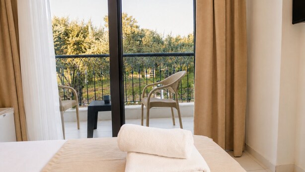 A hotel room with a bed, a chair, a table, and a view of the outdoors. - Kent Otel Ayvalık (Ayvalik)