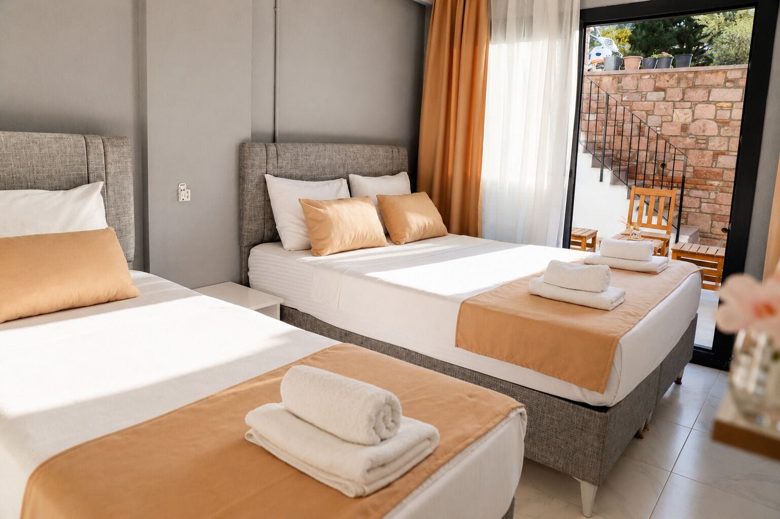 Ein Hotelzimmer mit zwei Betten, einem Balkon mit Steinwand und Blick ins Freie.